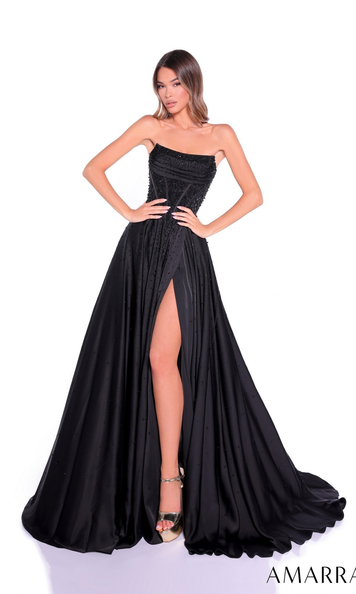 A woman stands with hands on hips against a white background, wearing the Amarra 89387 long prom dress featuring a strapless satin design, rhinestone corset bodice, and high-leg slit.